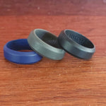 Beveled Edge silicone wedding rings in blue, grey and black on timber