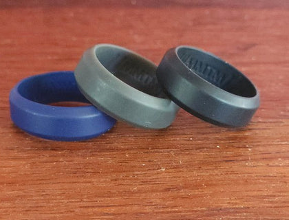 Beveled Edge silicone wedding rings in blue, grey and black on timber